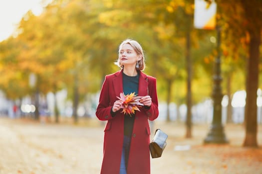 Beautiful young woman with bunch of colorful autumn leaves walking in park on a fall day