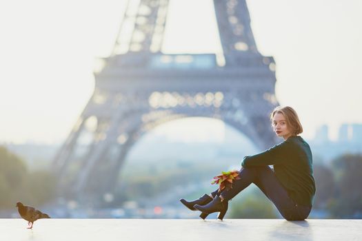 Beautiful young French woman with bunch of colorful autumn leaves near the Eiffel tower in Paris on a fall day