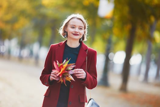 Beautiful young woman with bunch of colorful autumn leaves walking in park on a fall day
