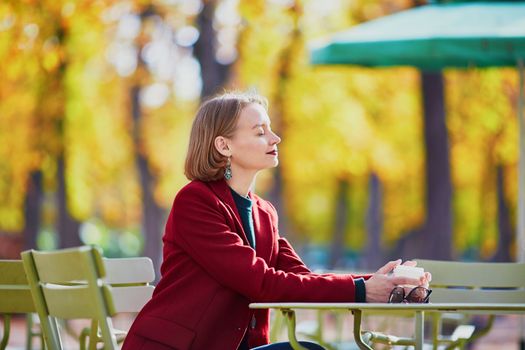 Elegant Parisian woman drinking coffee in park on a bright sunny autumn day