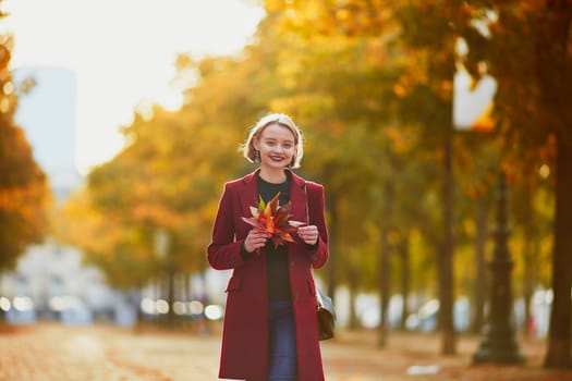 Beautiful young woman with bunch of colorful autumn leaves walking in park on a fall day