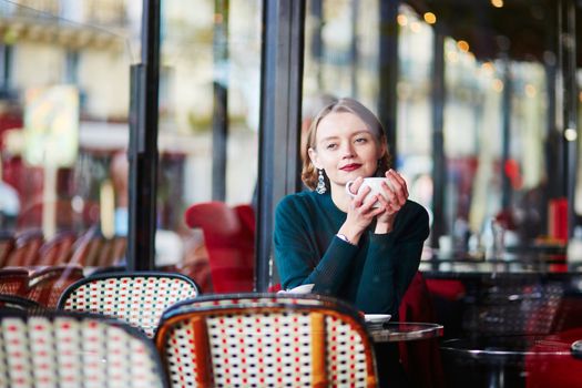 Elegant French woman drinking coffee in Parisian cafe near the window