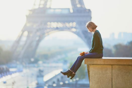 Beautiful young French woman with bunch of colorful autumn leaves near the Eiffel tower in Paris on a fall day