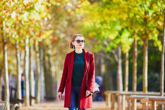 Beautiful young woman with bunch of colorful autumn leaves walking in park on a fall day. Luxembourg garden, Paris, France