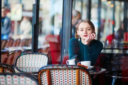 Young elegant woman drinking coffee and using her mobile phone in traditional cafe in Paris, France