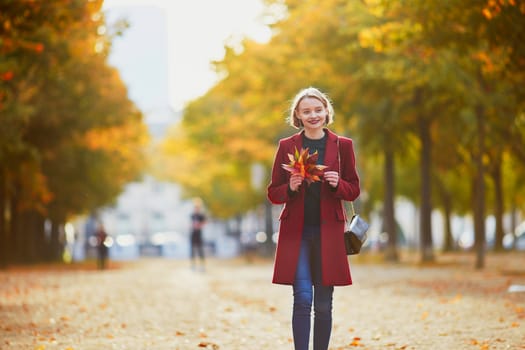 Beautiful young woman with bunch of colorful autumn leaves walking in park on a fall day