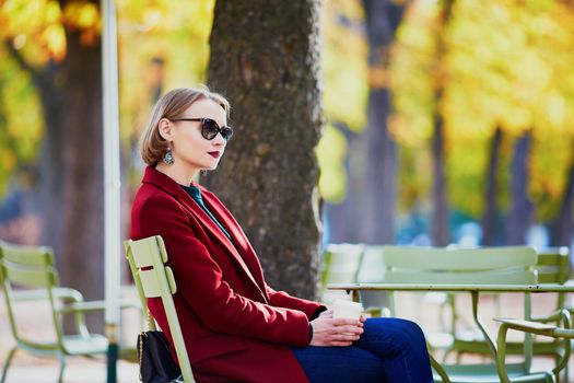 Elegant Parisian woman drinking coffee in park on a bright sunny autumn day