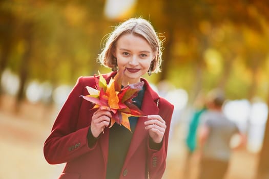 Beautiful young woman with bunch of colorful autumn leaves walking in park on a fall day