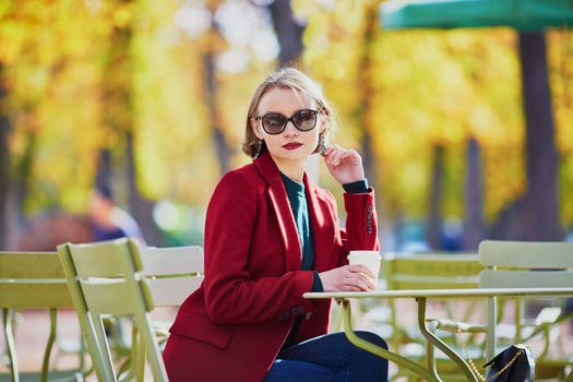 Elegant Parisian woman drinking coffee in park on a bright sunny autumn day