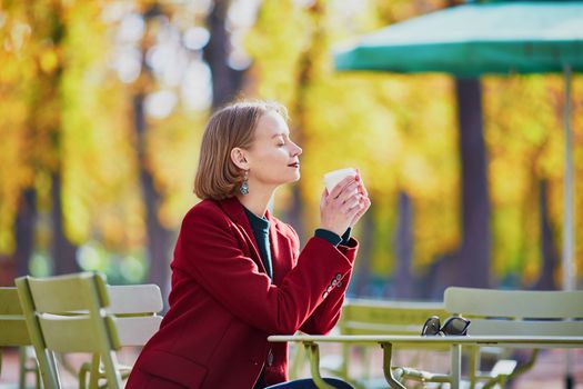 Elegant Parisian woman drinking coffee in park on a bright sunny autumn day