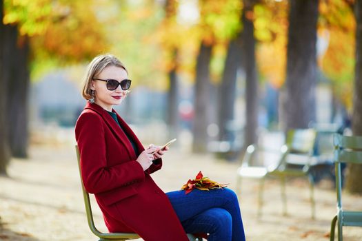 Elegant Parisian woman using her mobile phone in park on a bright sunny autumn day