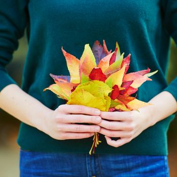 Beautiful young woman with bunch of colorful autumn leaves walking in park on a fall day. Luxembourg garden, Paris, France