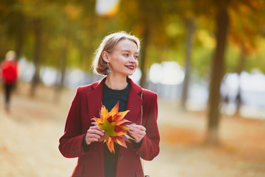Beautiful young woman with bunch of colorful autumn leaves walking in park on a fall day