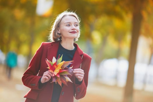 Beautiful young woman with bunch of colorful autumn leaves walking in park on a fall day