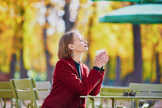 Elegant Parisian woman drinking coffee in park on a bright sunny autumn day