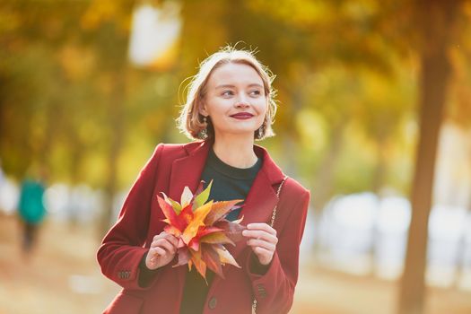 Beautiful young woman with bunch of colorful autumn leaves walking in park on a fall day