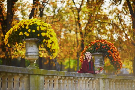 Beautiful young woman with bunch of colorful autumn leaves walking in park on a fall day. Luxembourg garden, Paris, France