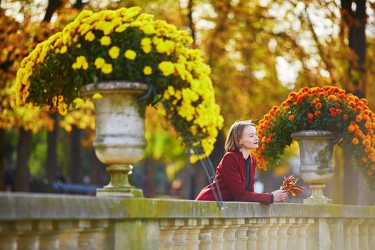 Beautiful young woman with bunch of colorful autumn leaves walking in park on a fall day. Luxembourg garden, Paris, France