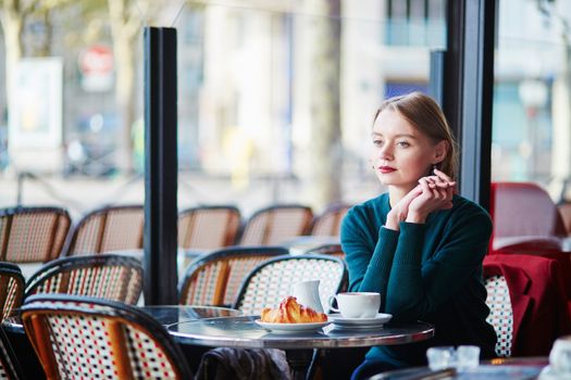 Elegant French woman drinking coffee in Parisian cafe near the window