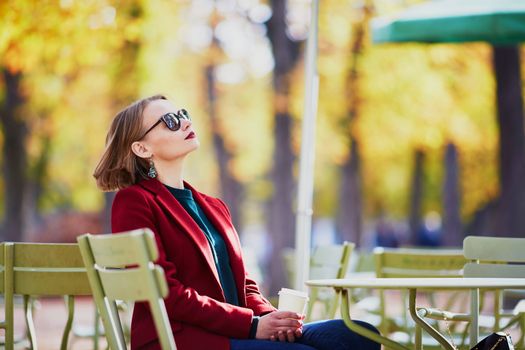 Elegant Parisian woman drinking coffee in park on a bright sunny autumn day