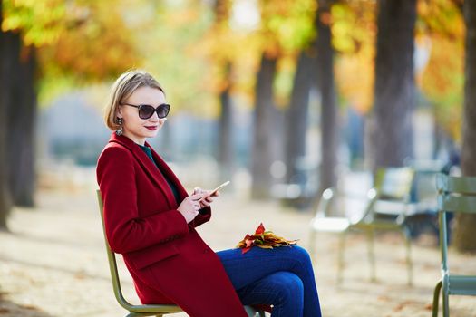 Elegant Parisian woman drinking coffee in park on a bright sunny autumn day