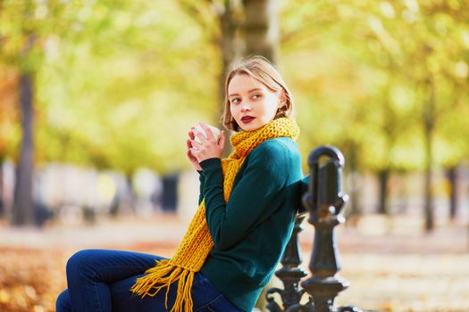 Happy young girl in yellow scarf with coffee to go walking in autumn park on a bright fall day