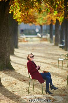 Elegant Parisian woman using her mobile phone in park on a bright sunny autumn day