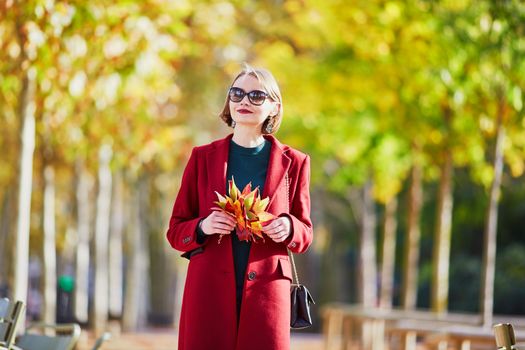 Beautiful young woman with bunch of colorful autumn leaves walking in park on a fall day. Luxembourg garden, Paris, France