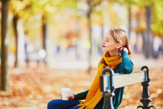 Happy young girl in yellow scarf with coffee to go walking in autumn park on a bright fall day