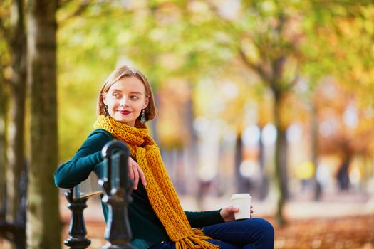 Happy young girl in yellow scarf with coffee to go walking in autumn park on a bright fall day