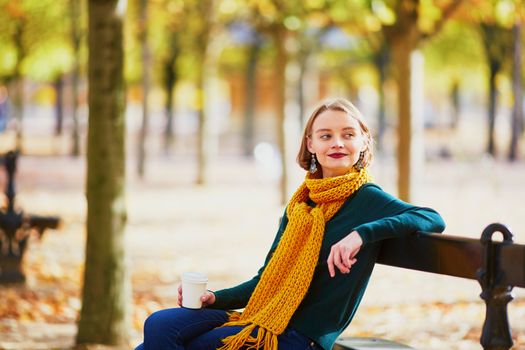 Happy young girl in yellow scarf with coffee to go walking in autumn park on a bright fall day