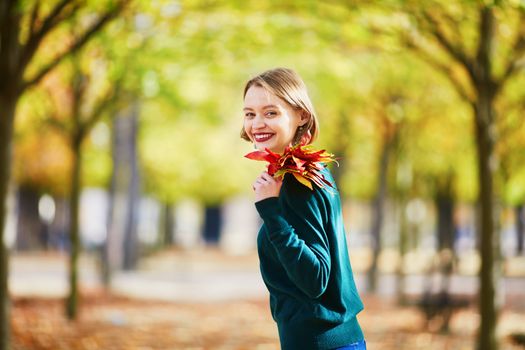 Beautiful young woman with bunch of colorful autumn leaves walking in park on a fall day. Luxembourg garden, Paris, France