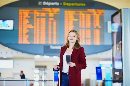 Young woman in international airport with luggage and coffee to go waiting for her flight
