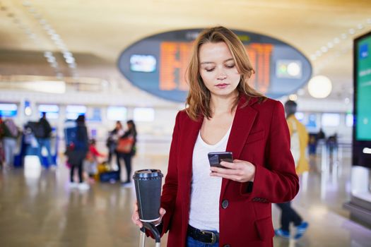 Young woman in international airport with luggage and coffee to go waiting for her flight