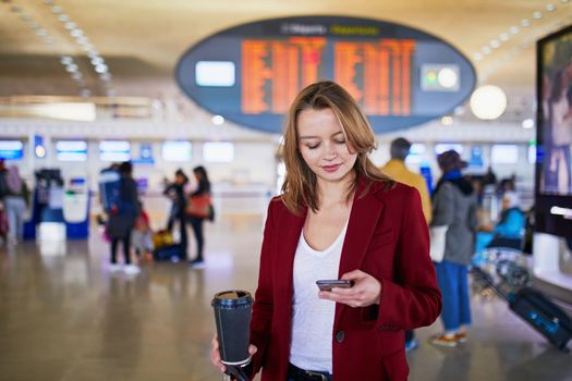 Young woman in international airport with luggage and coffee to go waiting for her flight