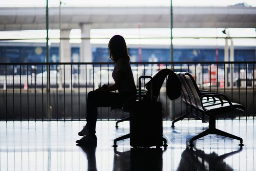 Silhouette of young woman in international airport sitting and waiting for her flight.