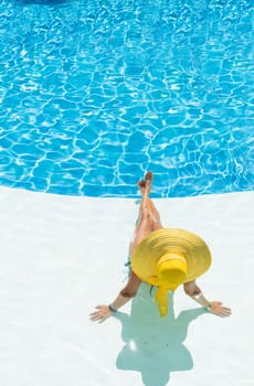 beautiful woman in a hat sitting on the edge of the swimming pool