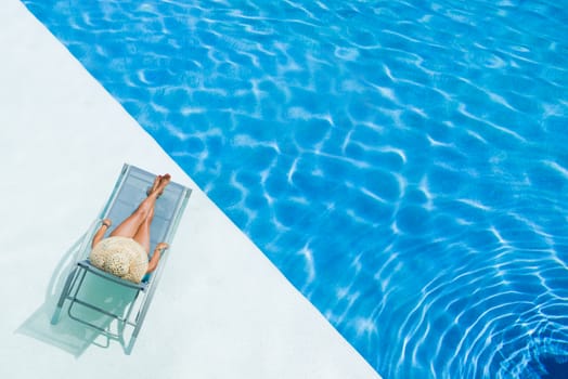 beautiful woman in a hat sitting on the edge of the swimming pool