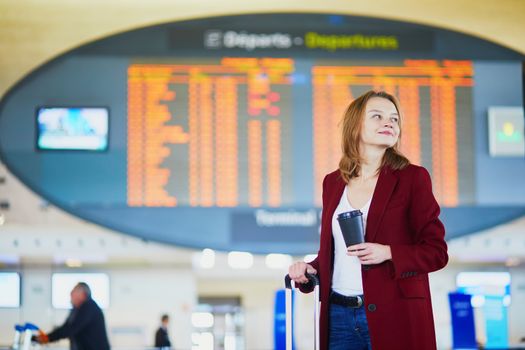 Young woman in international airport with luggage and coffee to go waiting for her flight