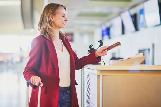 Young woman in international airport at check-in counter giving her passport to officer