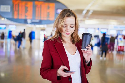 Young woman in international airport with luggage and coffee to go waiting for her flight