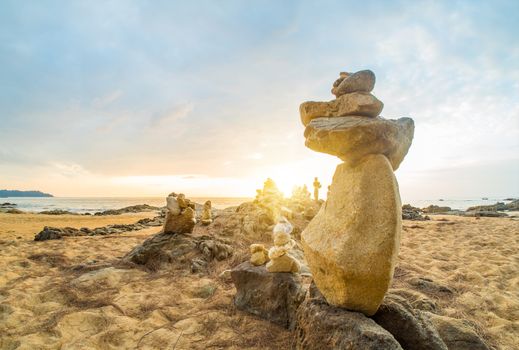 Stones pyramid on sand symbolizing zen, harmony, balance. Ocean at sunset in Khao Lak Thailand