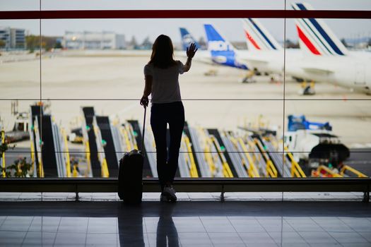 Silhouette of young woman in international airport, looking through the window at planes