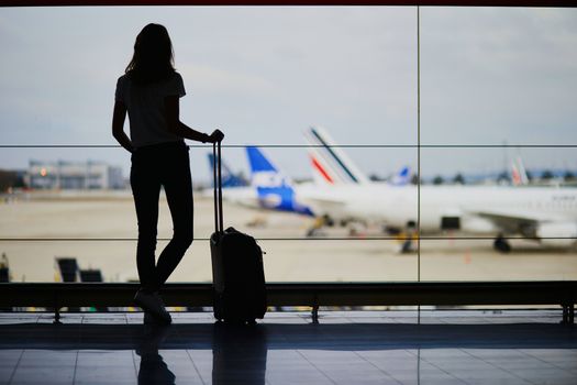 Silhouette of young woman in international airport, looking through the window at planes