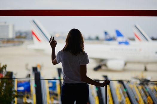 Silhouette of young woman in international airport, looking through the window at planes