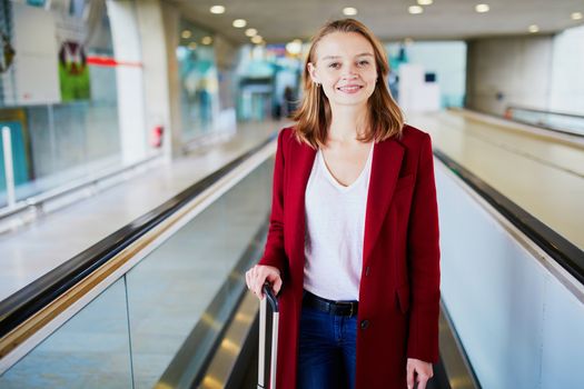 Young woman in international airport with luggage on travelator