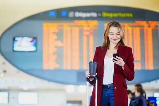 Young woman in international airport with luggage and coffee to go waiting for her flight