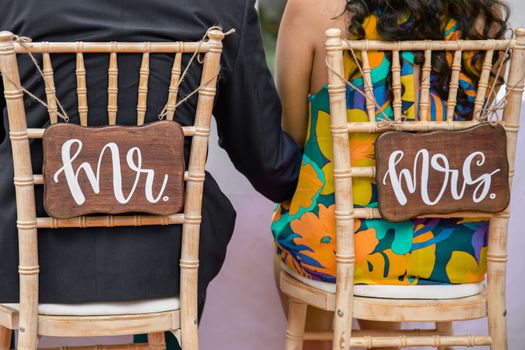 Bride and groom sitting in Mr and Mrs wedding chairs during a wedding ceremony