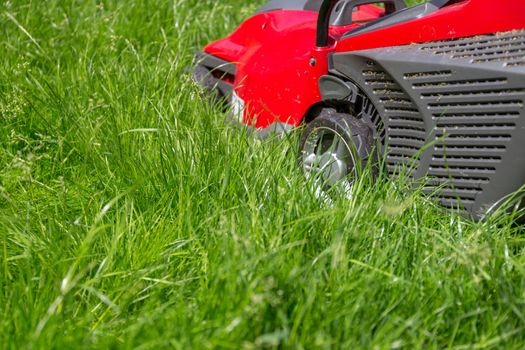 A close up image of a lawnmower on a lawn of long grass in need of cutting