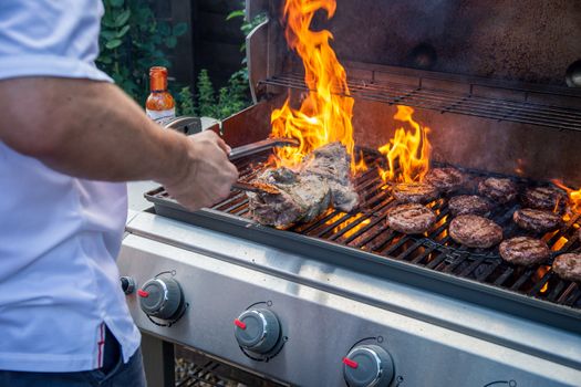 Marinated lamb joint and beef burgers cooking on a barbecue